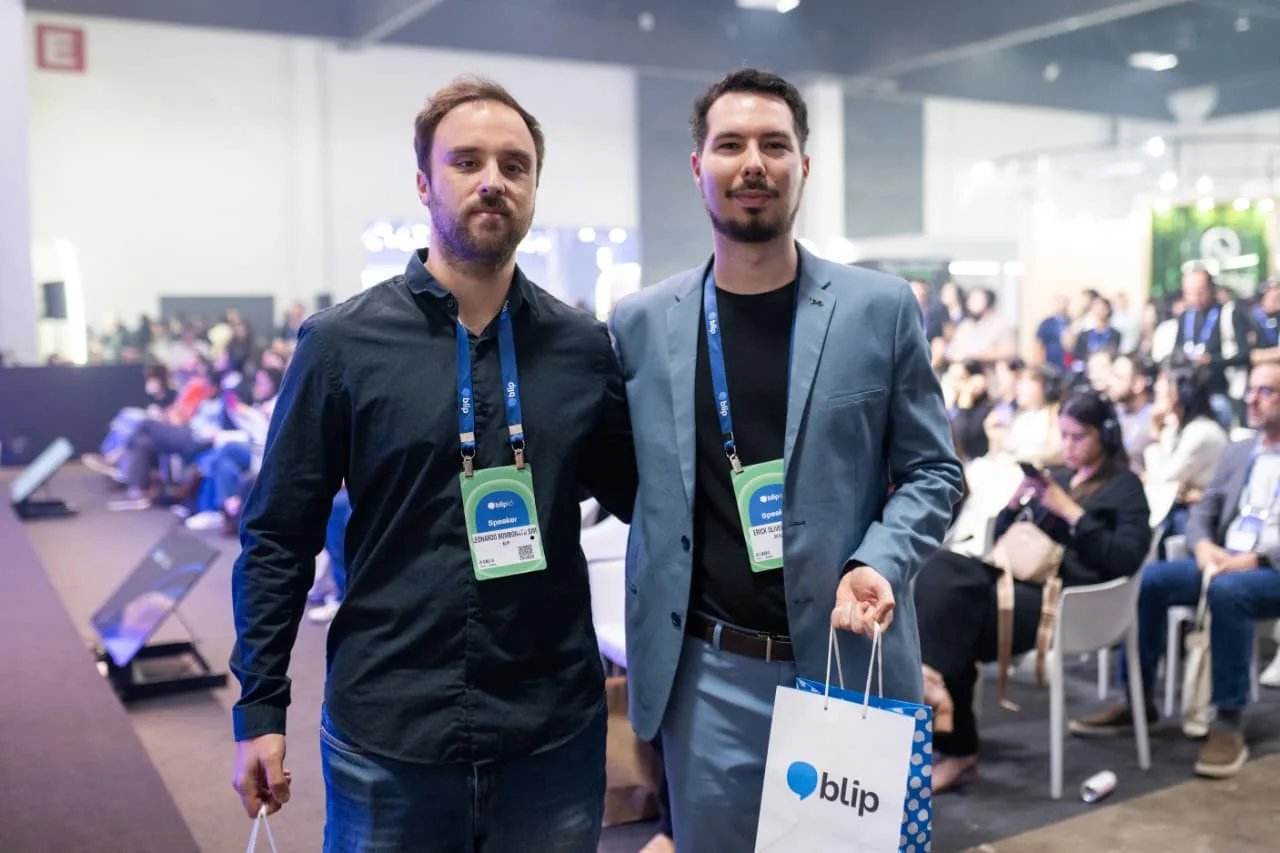 Two team members with badges and a Blip bag at an event, audience in the background