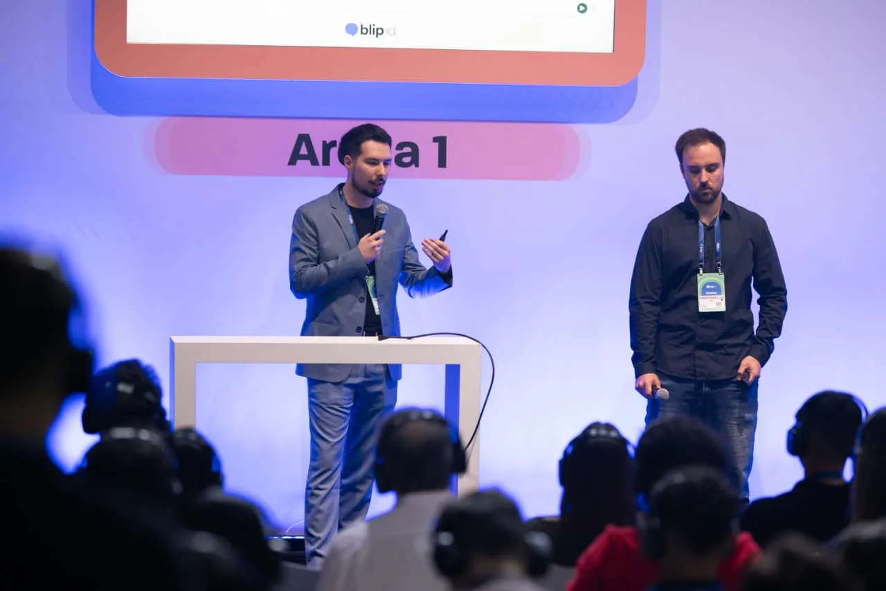 Two team members presenting on the Arena 1 stage, with the audience wearing headphones