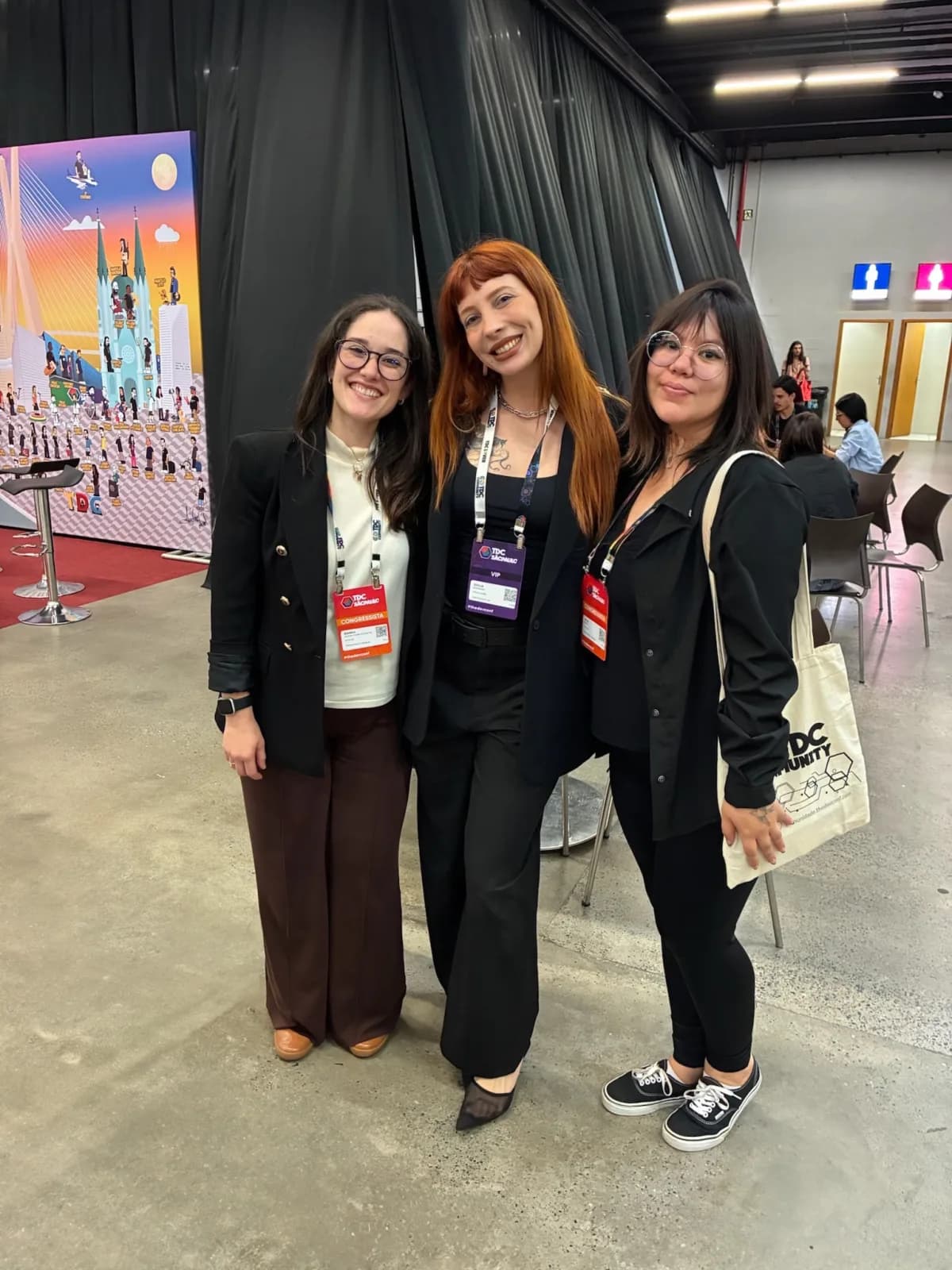 Three team members wearing badges at The Developer's Conference, one of them with the TDC Community tote bag